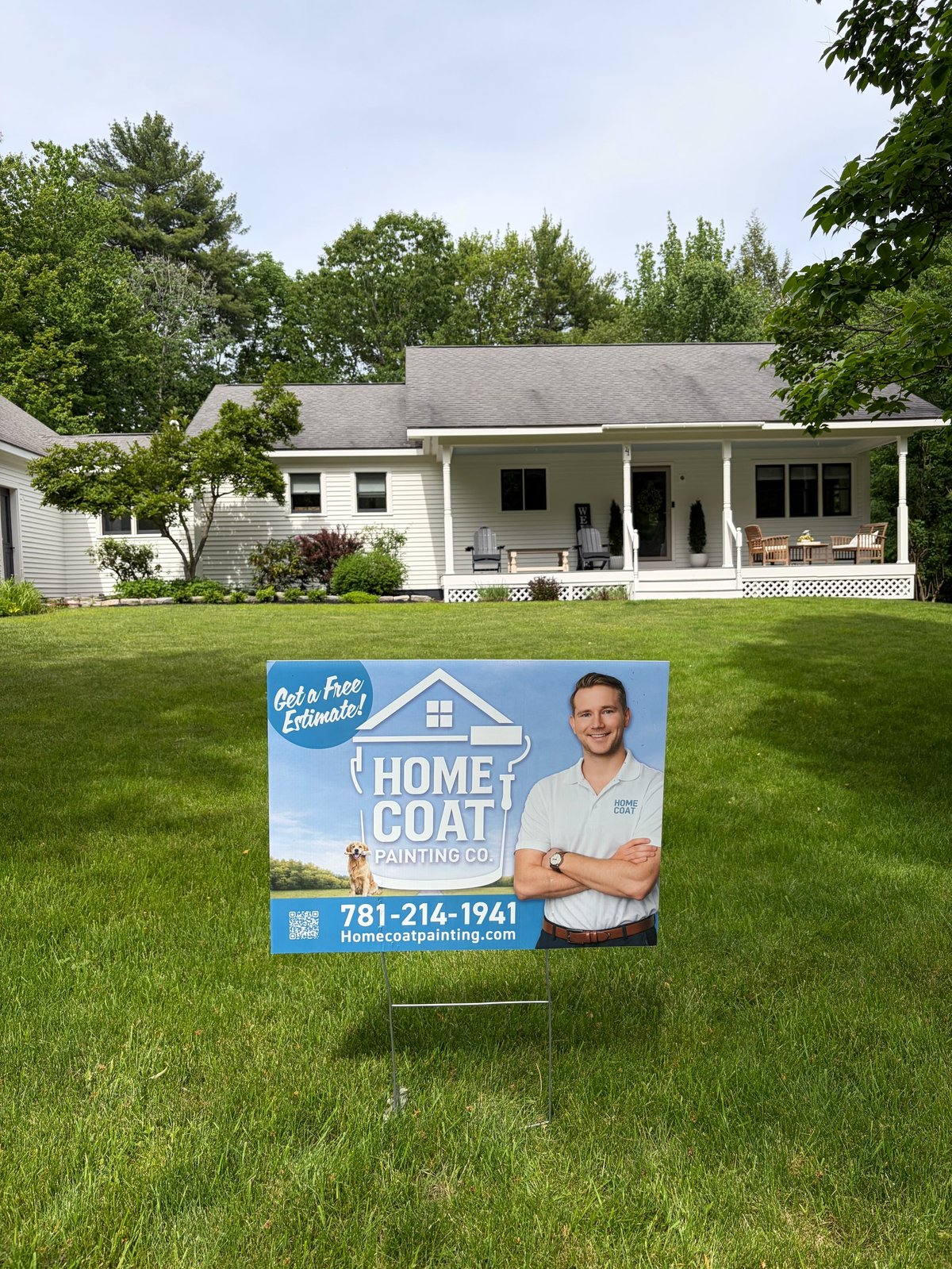 Real estate yard sign for Home Coat Painting Co. displayed on lawn in front of white house with porch